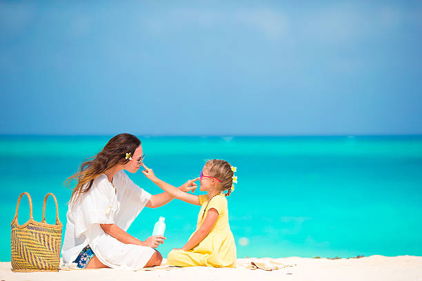 маленький привлекательная девочка, применяя солнце крем на носу ее мать - beach sand стоковые фото и изображения