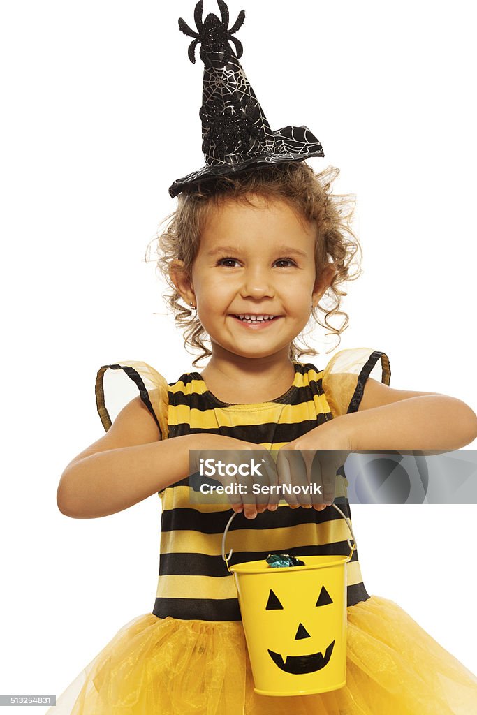Little girl in bee costume with Halloween bucket Nice beautiful little girl with curly hair and bucket with candies standing isolated no white in Halloween hat with spider Autumn Stock Photo
