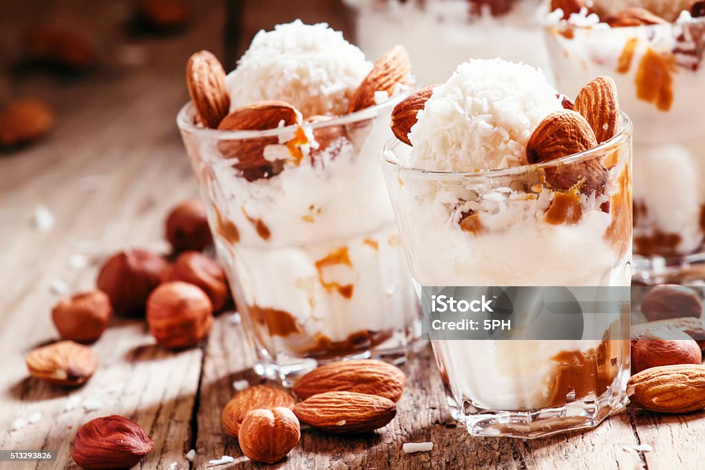 Dessert with vanilla ice cream, nut sauce, almond Dessert with vanilla ice cream, nut sauce, almonds, hazelnuts and coconut, served in glasses, selective focus Caramel Stock Photo
