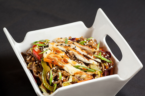 Asian noodles wok with omelette and vegetables on dark background