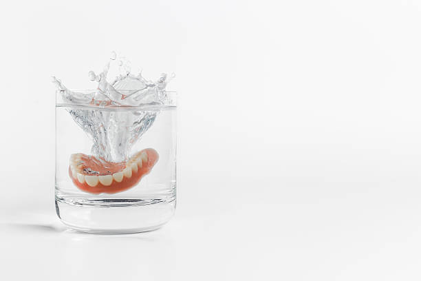 Dentures splashing in glass of water Single orthodontic dentures mold falling into clear glass of water with splash over white background next to copy space on side dentures stock pictures, royalty-free photos & images