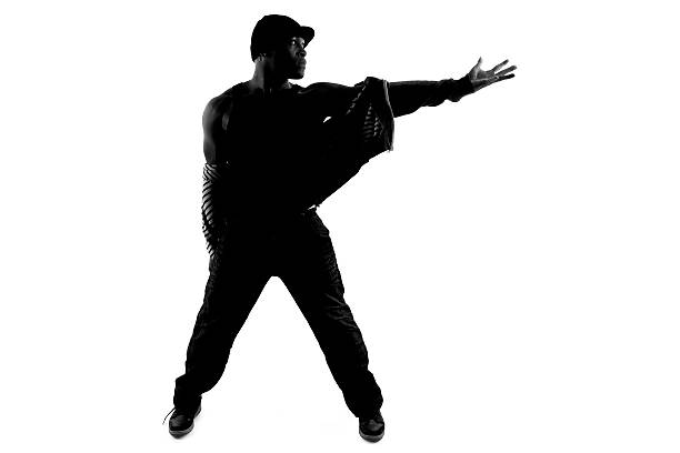 Black and white silhouette of a male dancer posing with dance moves.  He is backlit and partly in shadow to show of his body form.  The active performer is on a white background.  He is showing off his hip hop dance style.