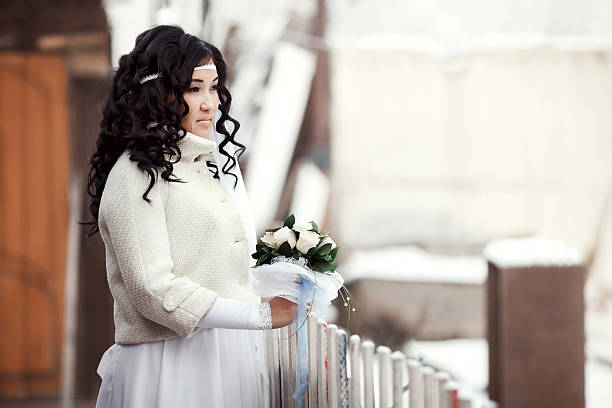 Asian bride in a winter coat standing outdoors looks into stock photo