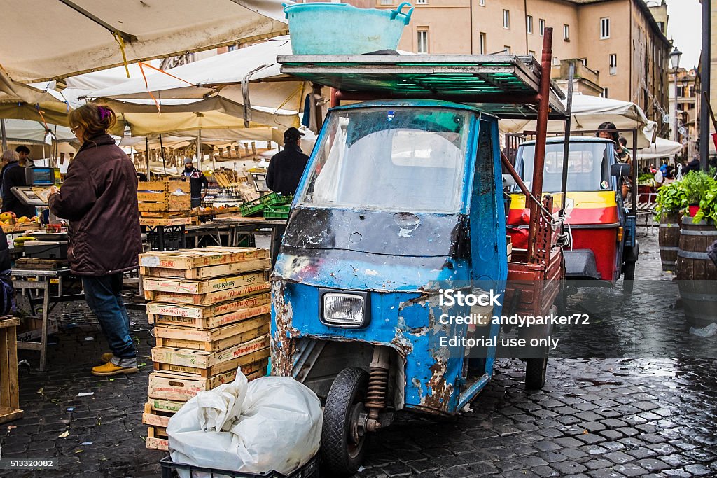 People, boxes and three-wheeled vans in Campo de Fiori Rome, Italy - 27 February 2016:  View of people selling produce from the market in the Campo dei Fiori with stacked boxes and the typical three-wheeled transportation vans parked behind the stalls. Image of contemporary Italian lifestyle and daily routine in Rome.   Beaten Up Stock Photo