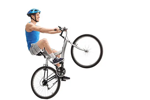 Young cyclist performing a wheelie with a bicycle isolated on white background