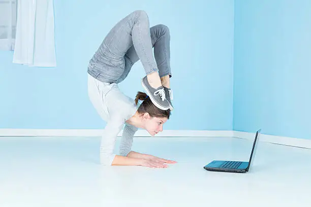 A female gymnast, fit and flexible, about to do some work on her laptop computer, whilst being a contortionist.