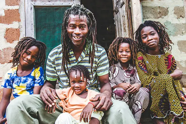 African rasta father sitting in front of their house with three daughters and one son.