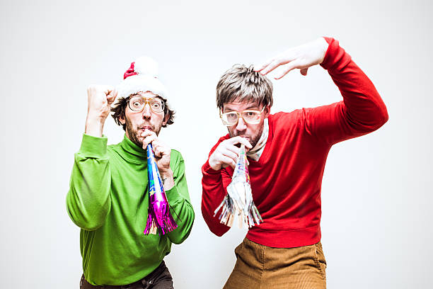 Christmas Nerds Two goofy looking men in ugly Christmas colored turtlenecks and sweaters blow party horns to celebrate Christmas or New Years.  Horizontal image. christmas ugliness sweater nerd stock pictures, royalty-free photos & images