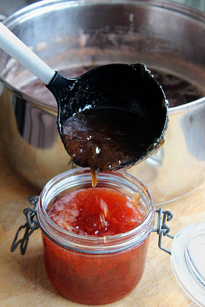 hot confiture de fraises être ladled en pots de verre de confiture stérilisé - ladled photos et images de collection