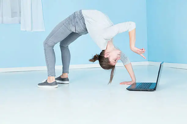 A female gymnast, fit and flexible, working on her laptop computer, whilst being a contortionist.