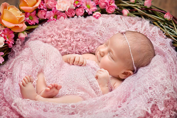 Little newborn girl 11 days, smiles. Beautiful newborn and flowers stock photo
