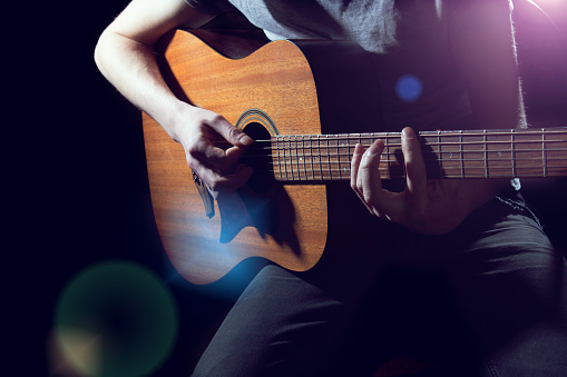 Musician playing on acoustic guitar on dark background
