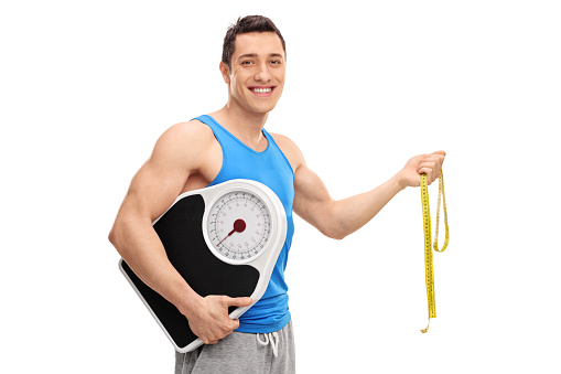 Cheerful athlete holding a weight scale and a measuring tape isolated on white background