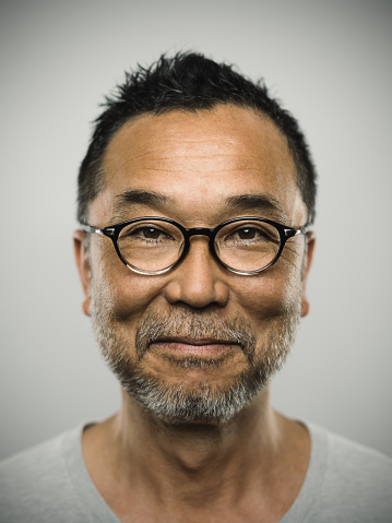 Studio portrait of a japanese mature man looking at camera with relaxed expression. The man has around 50 years and has glasses, short hair and a short grey beard. Vertical colour image from a medium format digital camera.