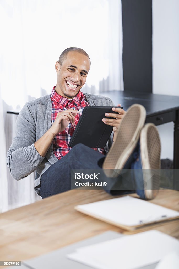 Young man with feet up Relaxed young man, 20s, mixed race African American / Caucasian, with feet up on table, using digital tablet. Business Stock Photo