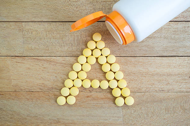 желтый таблетки образуя силуэт на деревянный фон с буквами алфавита - vitamin a стоковые фото и изображения
