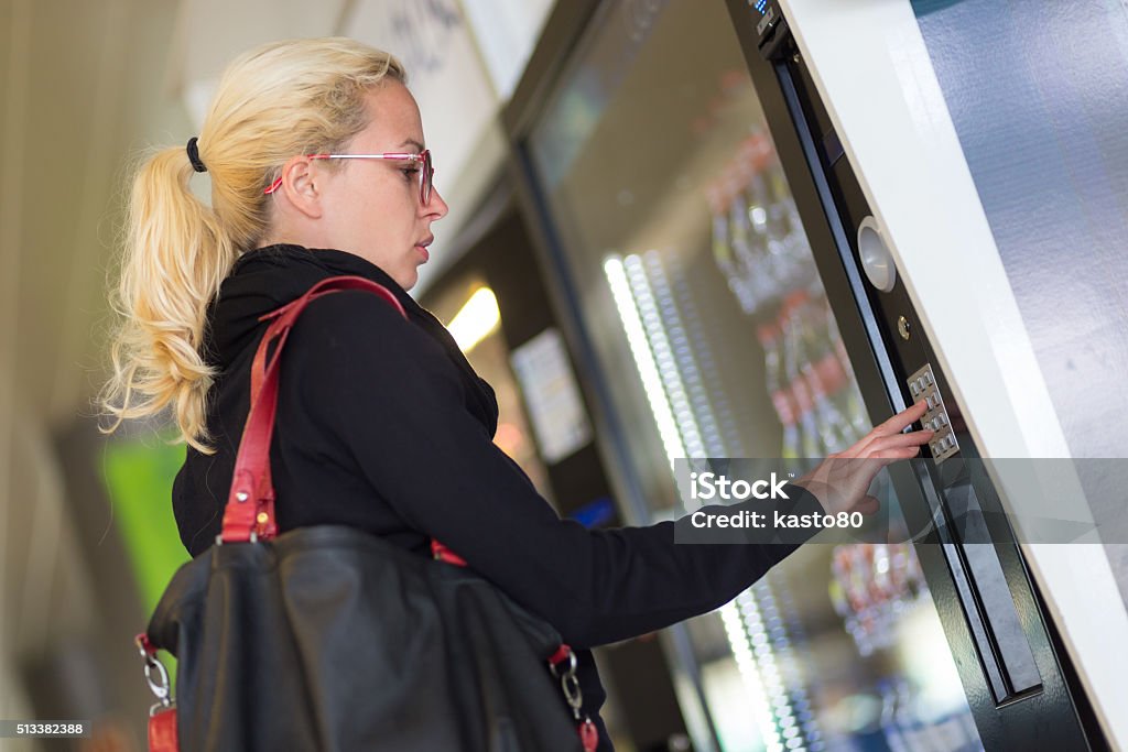 Lady using  a modern vending machine Casual caucasian woman using a modern beverage vending machine. Her hand is placed on the dial pad and she is looking on the small display screen. Vending Machine Stock Photo