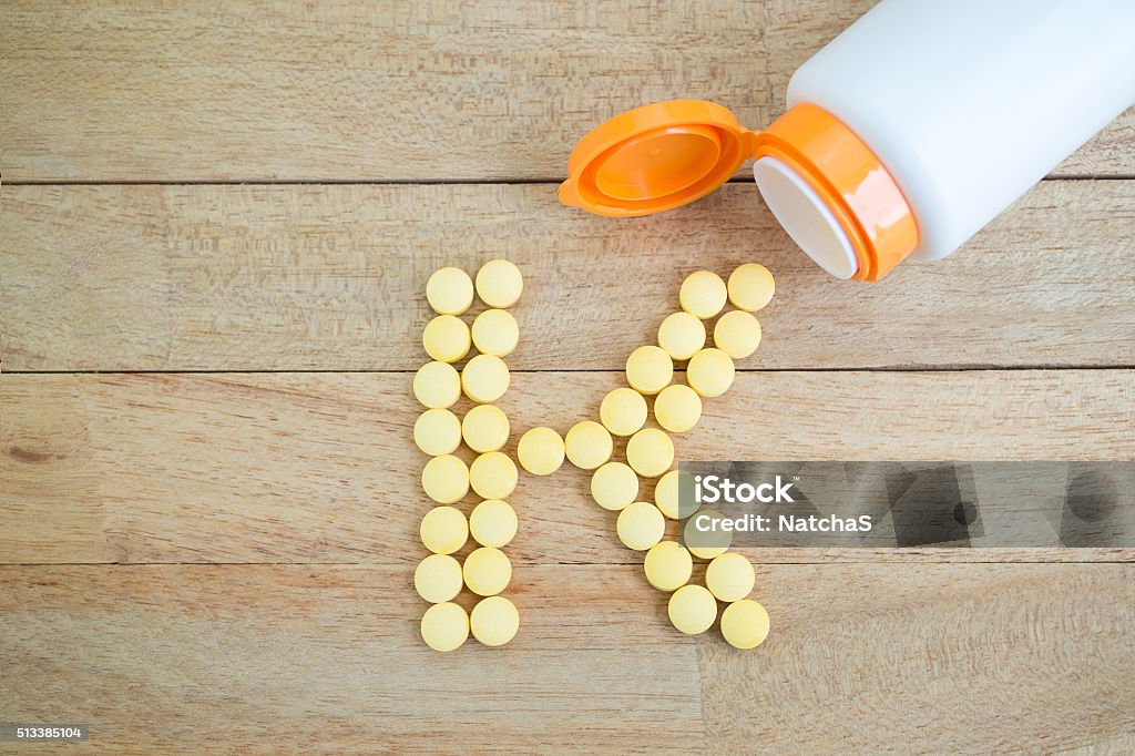 Yellow pills forming shape to K alphabet on wood background Letter K Stock Photo