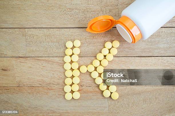 Yellow Pills Forming Shape To K Alphabet On Wood Background Stock Photo - Download Image Now