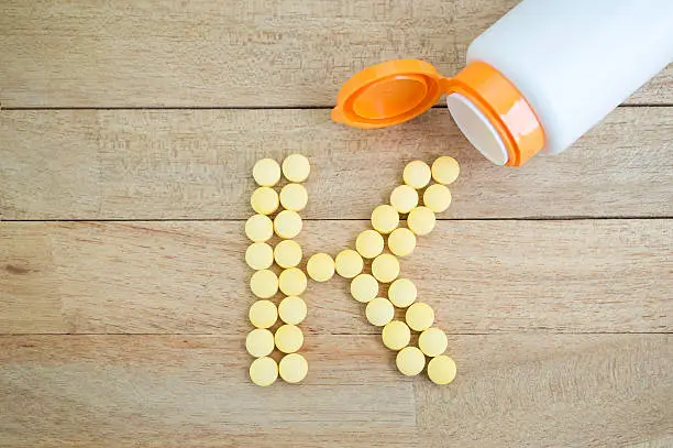 Yellow pills forming shape to K alphabet on wood background