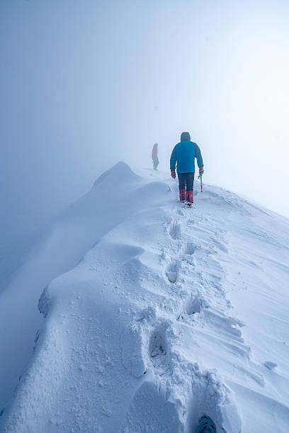 istock 2 men walking along snowy mountain peak into the clouds 513386644