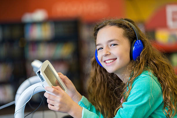 istock Elementary girl using digital tablet and headphones in modern library 513392740
