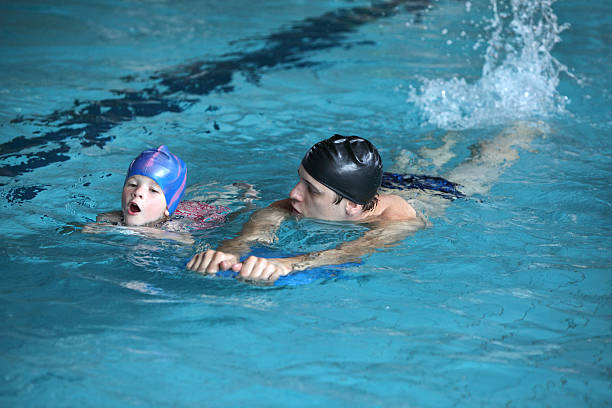 урок плавания ребенок, играющий на развевающиеся удар с тренером - swimming child swimming pool indoors стоковые фото и изображения