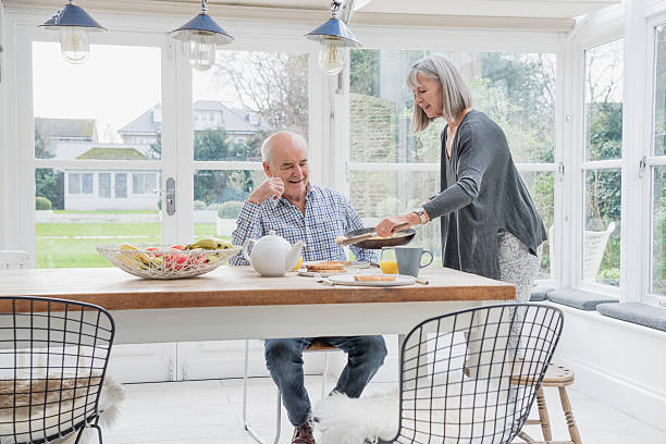 пожилая пара наслаждаясь завтрак в обеденным столом - indoors conservatory decor home interior стоковые фото и изображения