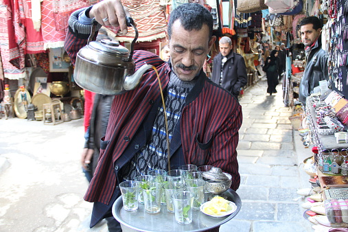 Tunis, Tunisia - February 4, 2013: street vendor pouring traditional Tunisian green tea for customers in Old Town market, Tunis, Tunisia.