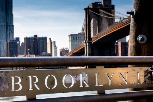 A Brooklyn Bridge Sign, with the Brooklyn Bridge in the background.