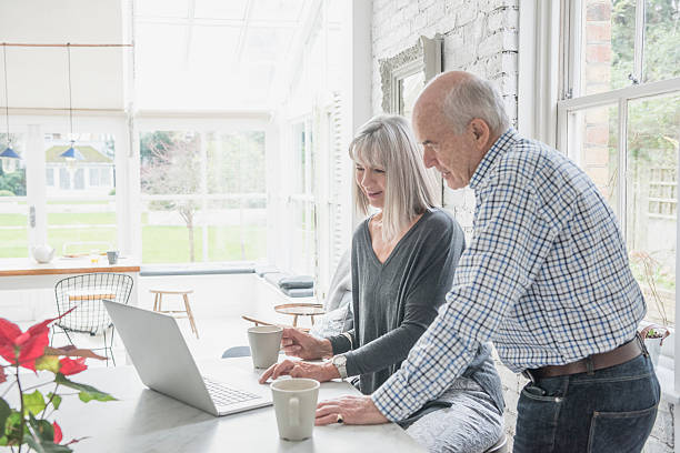 Two seniors using a laptop at home in modern conservatory