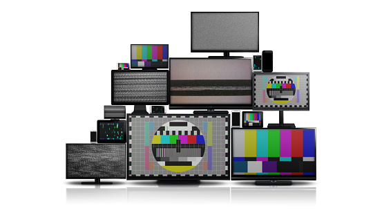 Many different types of screens. TVs, computer monitors, smartphones and tablets. They laid on each other in a pile isolated on a white background. They are all with no signal.