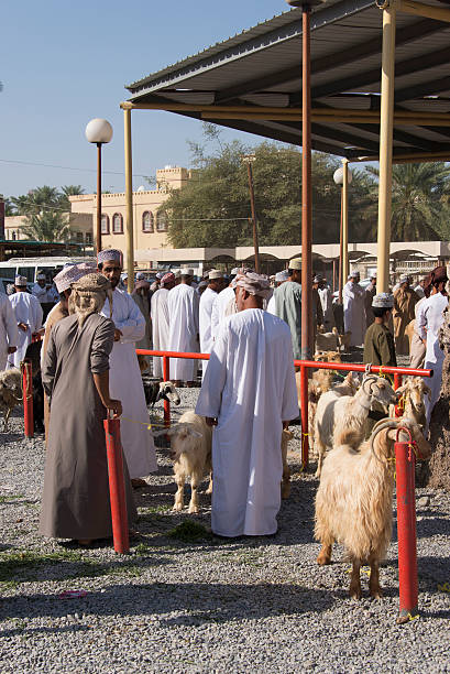 Nizwa, Oman - February 26, 2016: Omani and bedouin people in traditional costume chatting and looking at some goats at the local goat market in Nizwa, the former capital of Oman.