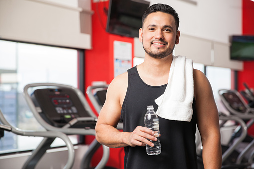 Portrait of a Hispanic young man taking a break and drinking some water after exercising in a gym