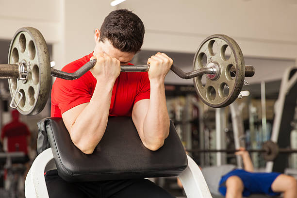 Young man in a preacher bench at the gym Young athletic man lifting a barbell on a preacher bench at the gym bent photos stock pictures, royalty-free photos & images