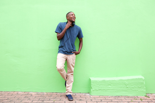 Full length portrait of stylish young african man standing against a green wall and looking away