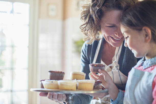 großmutter bietet enkelin cupcakes an - grandmother cooking baking family stock-fotos und bilder