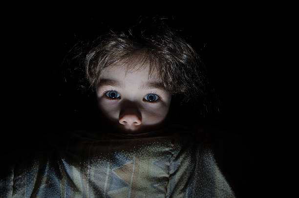 Powerful low key image of little girl in dark side with shadow on face with blissful eyes  looking up dreaming or praying.  Indoor portrait with natural light coming from a window