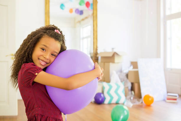 A young boy smiles joyously while holding a light blue balloon, sitting outdoors surrounded by whimsical party decorations