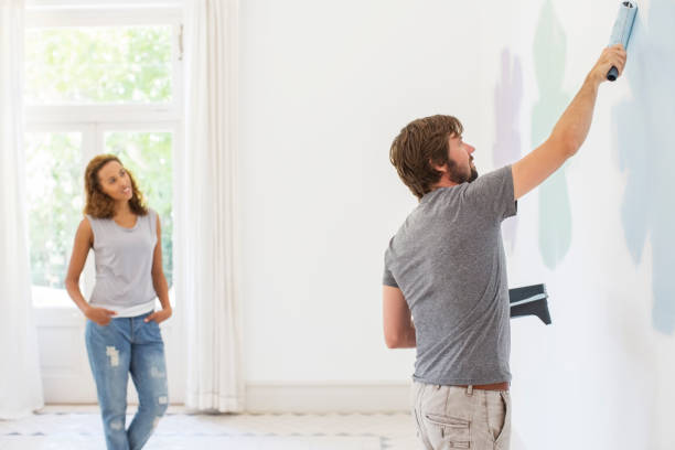 istock Man painting wall with girlfriend observing 513438703