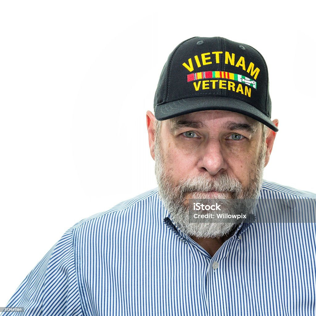Vietnam War Military Veteran Senior Adult Businessman A real person senior adult businessman authentic United States Vietnam War U. S. Navy military veteran dressed in a blue pin striped button down business shirt is looking at the camera with a serious facial expression. He has a gray beard and mustache and green eyes. He's wearing a very common, inexpensive, unbranded, generic souvenir shop military veteran commemorative baseball style cap with generic wording and simple replica campaign ribbon iron-on patch(es). Active Seniors Stock Photo