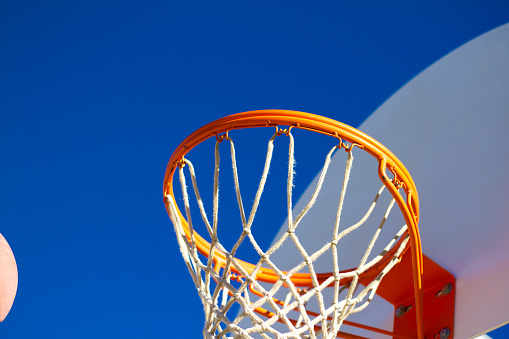 Scoring: a basketball just entering the frame and perhaps heading into a bright basketball hoop against an indigo sky (close-up). Vibrant colors. Copy space available.