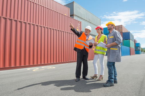 Thre colleagues discuss a shipping container consignment at commercial docks.