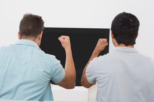 Rear view of two excited soccer fans watching tv