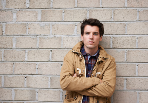 Cropped shot of a young man leaning against a brick wall with his arms crossed