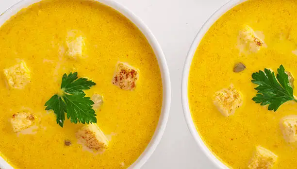 Two bowls of pumpkin soup with parsley leaf and croutons on white background close-up, top view with copy space