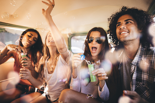 Group of multi-ethnical hipster friends having a funny soap bubbles party inside a vintage van to celebrate their road trip