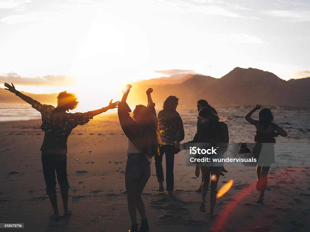 Teen friends dancing on the beach at sunset Fun loving friends having party on the beach and dancing with susnet sun flare Beach Stock Photo
