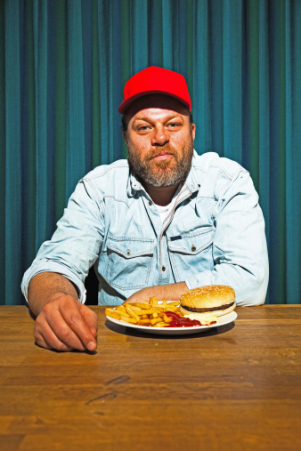 Man with beard eating fast food meal. Enjoying french fries and a hamburger. Trucker with red cap.