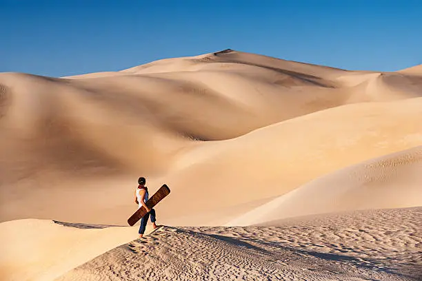 Young female sandboarding in The Sahara Desert. She is standing on a sand dune, and holding sandboard. The Sahara Desert is the world's largest hot desert with the biggest sand dunes.http://bem.2be.pl/IS/egypt_380.jpg